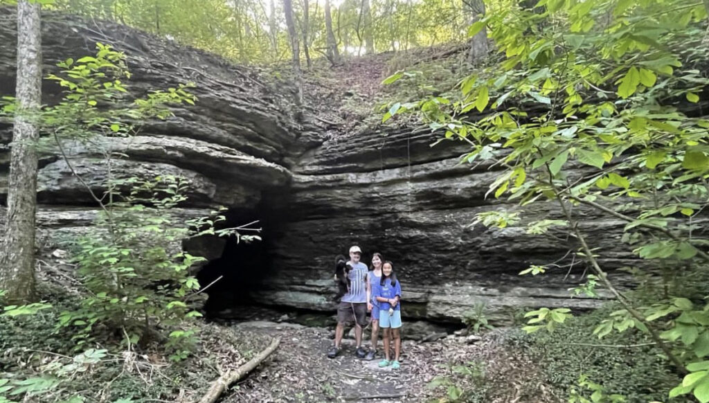 Family of 3 standing in front of 10 foot tall cave opening