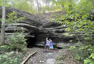 Family of 3 standing in front of 10 foot tall cave opening